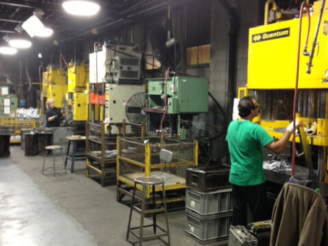 Carpenter Die Casting Workers operate large industrial machines in a factory setting, with metal components, tools, and safety equipment visible throughout the workspace.