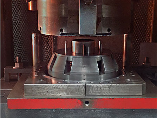 Carpenter Die Casting A close-up view of a metal forming press machine shaping a cylindrical metal workpiece.