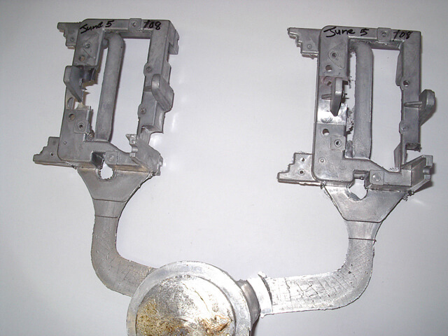 Carpenter Die Casting Two metal die-cast parts connected by a central channel, each part labeled "June 5" and "708" on the top edge, placed on a plain white background.