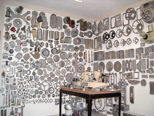Carpenter Die Casting A workshop wall covered with neatly organized metal parts and tools on pegboards, with a workbench and machinery in the foreground.