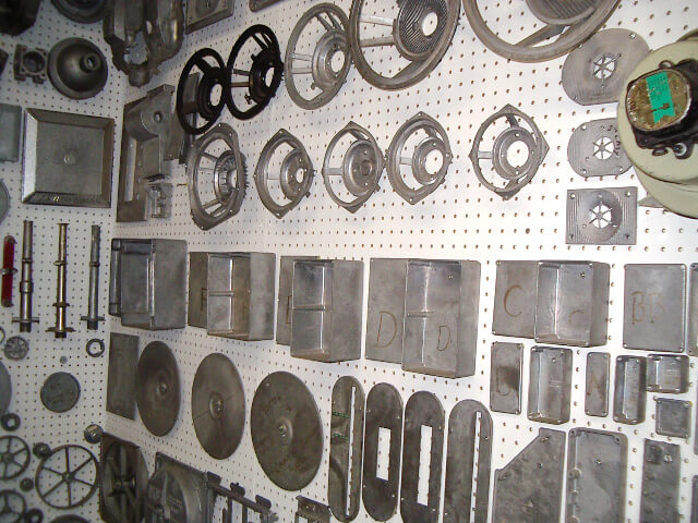 Carpenter Die Casting Assorted metal machine parts and components are neatly arranged on a white pegboard wall.