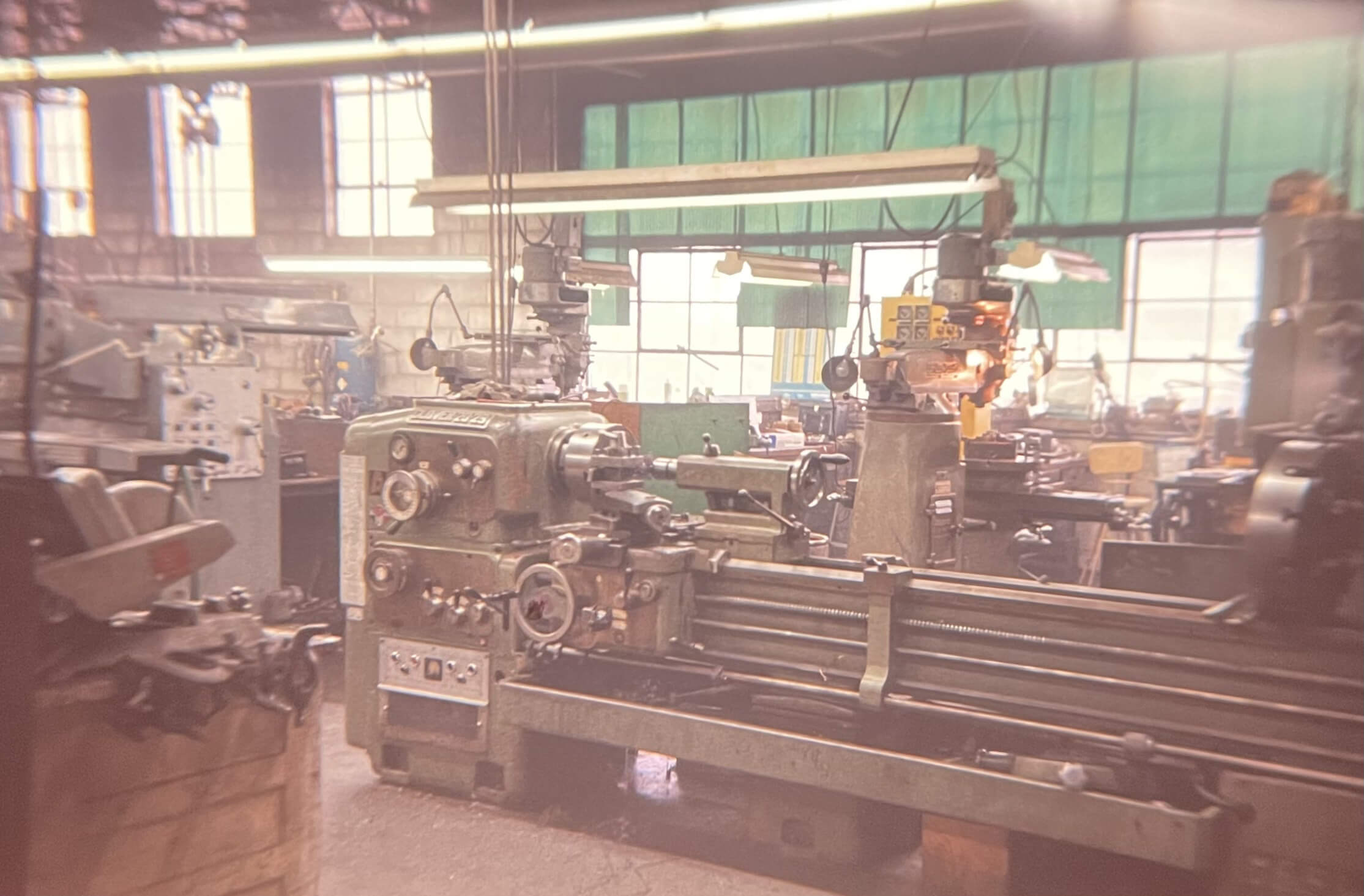 Carpenter Die Casting Industrial workshop with large metal lathe and other machining equipment, illuminated by overhead lights, with windows and green shades in the background.