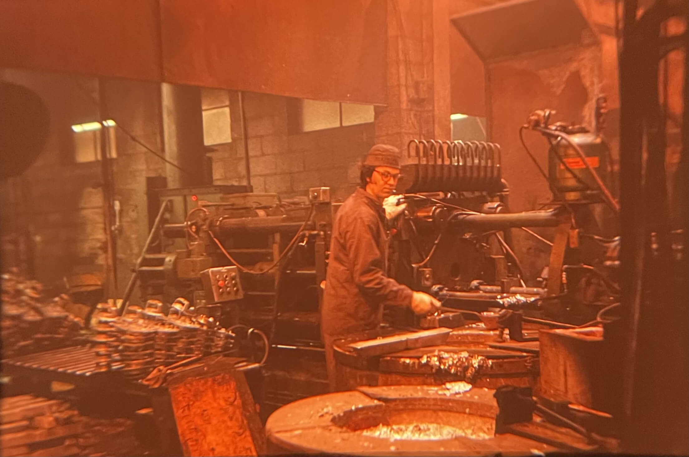 Carpenter Die Casting A factory worker operates machinery in an industrial workshop, surrounded by equipment and metal parts under warm, orange lighting.