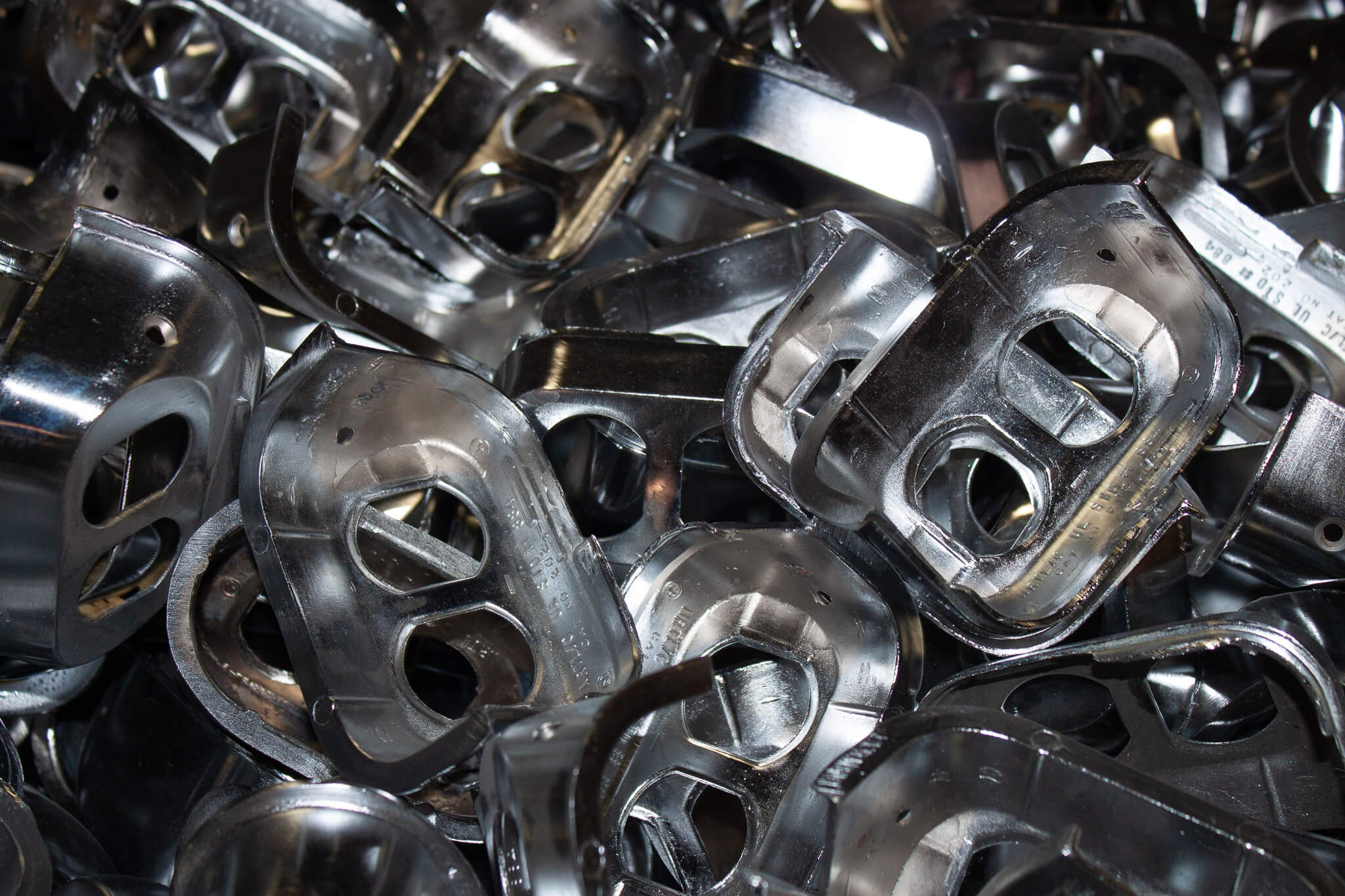 Carpenter Die Casting A pile of shiny, metal machine parts with various holes and cutouts, stacked closely together.