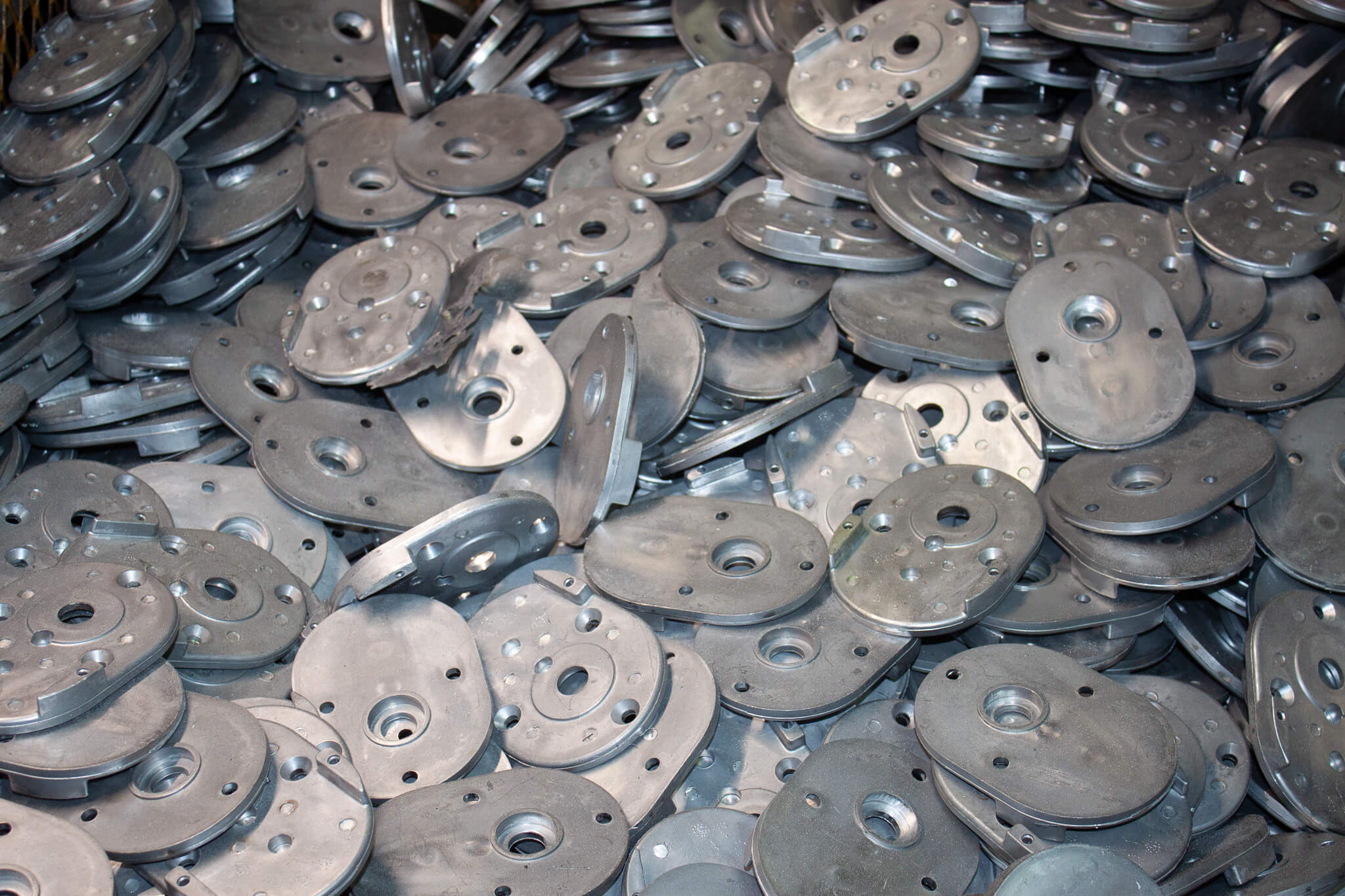 Carpenter Die Casting A large pile of oval-shaped metal parts with multiple holes, stacked closely together.