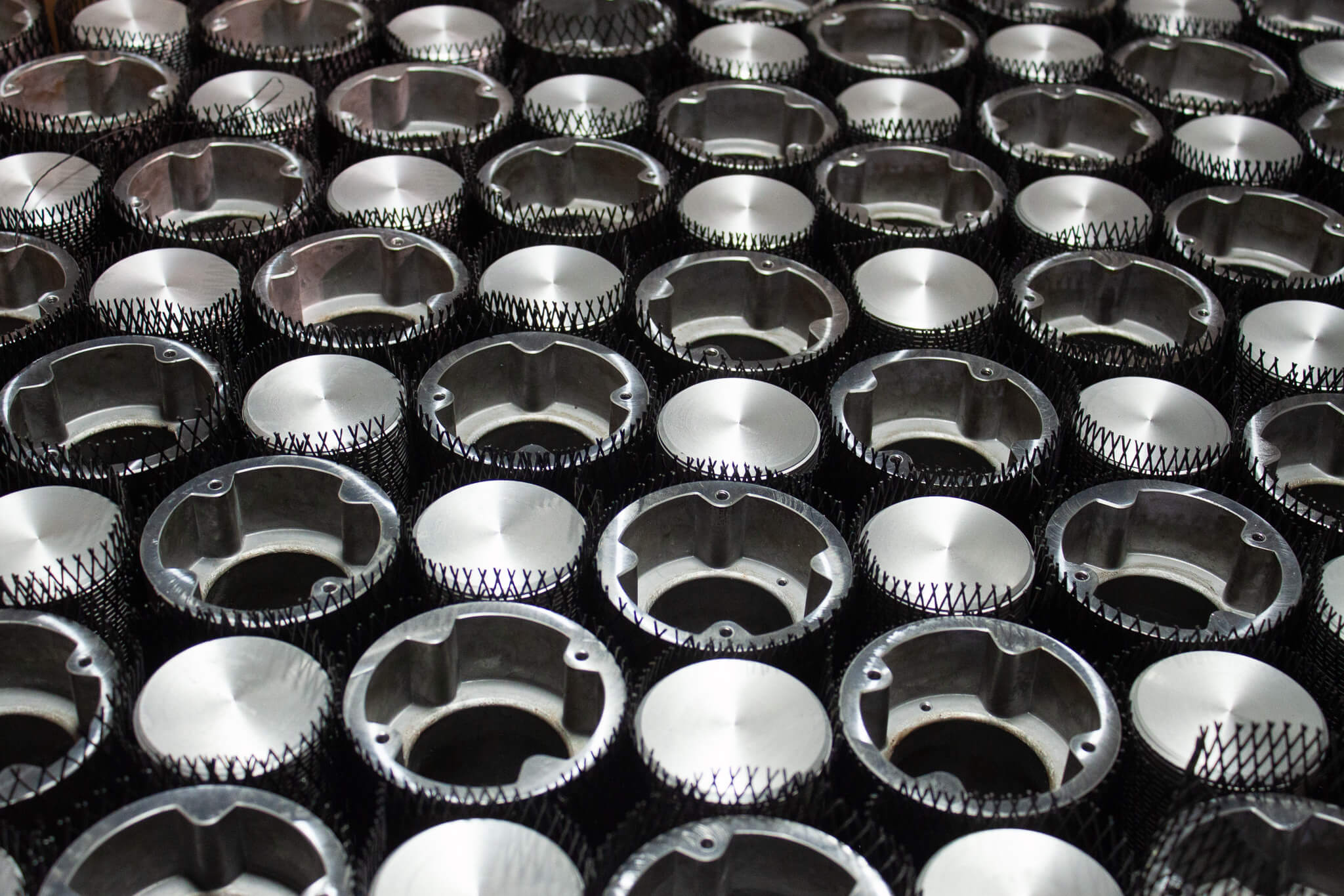 Carpenter Die Casting Rows of identical, shiny metal mechanical parts are arranged closely together, possibly components for machinery or engines.