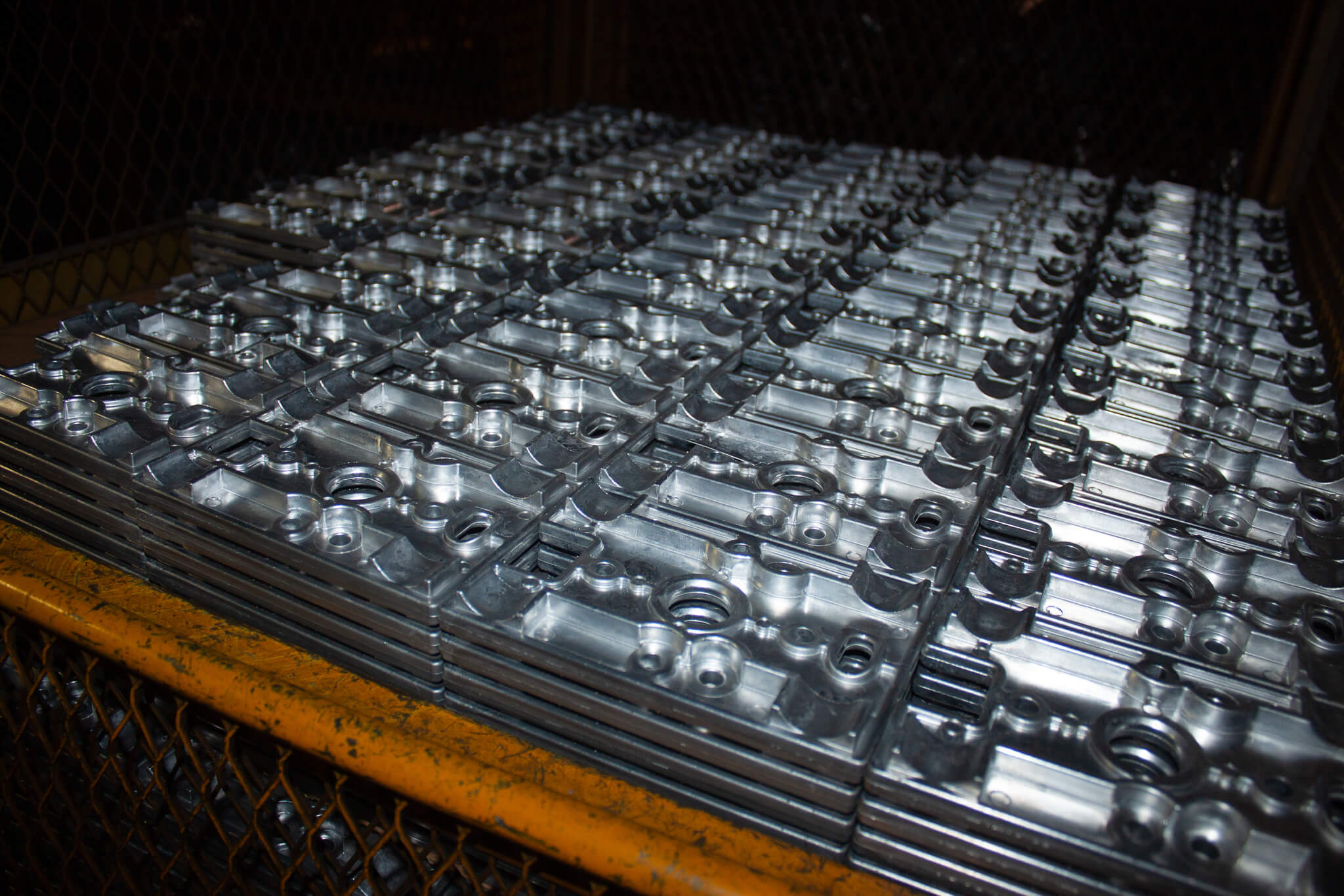 Carpenter Die Casting Stacks of identical machined metal parts arranged in rows on a metal tray inside an industrial setting.