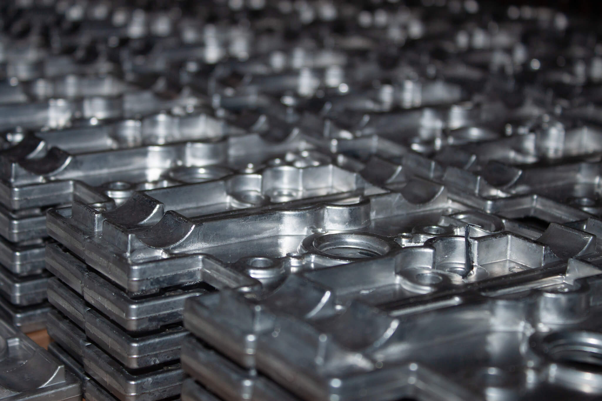 Carpenter Die Casting Stacks of machined metal parts with geometric patterns and holes, arranged closely together in rows.