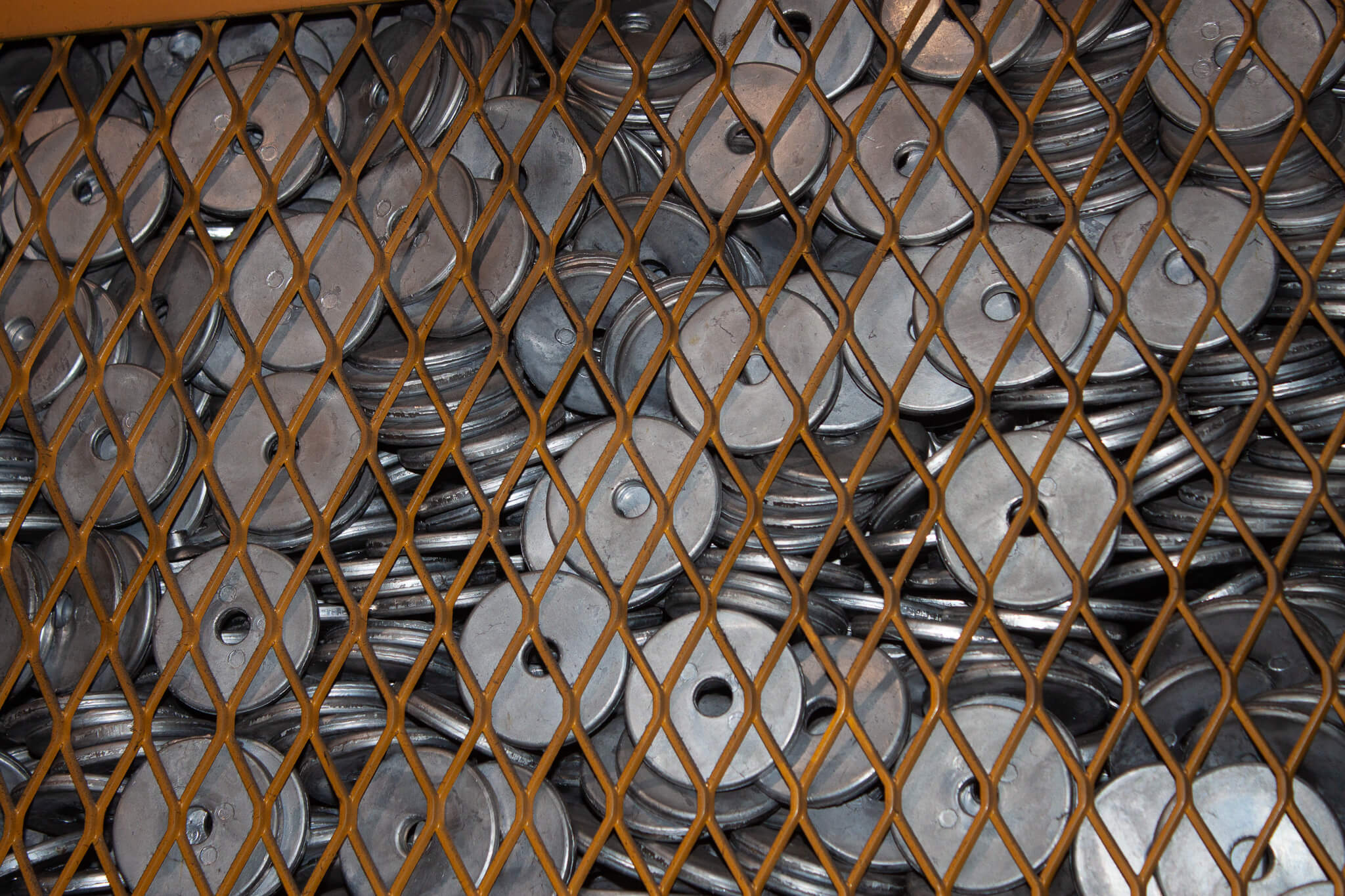Carpenter Die Casting A stack of round metal discs with holes in the center is seen behind a diamond-patterned metal grate.