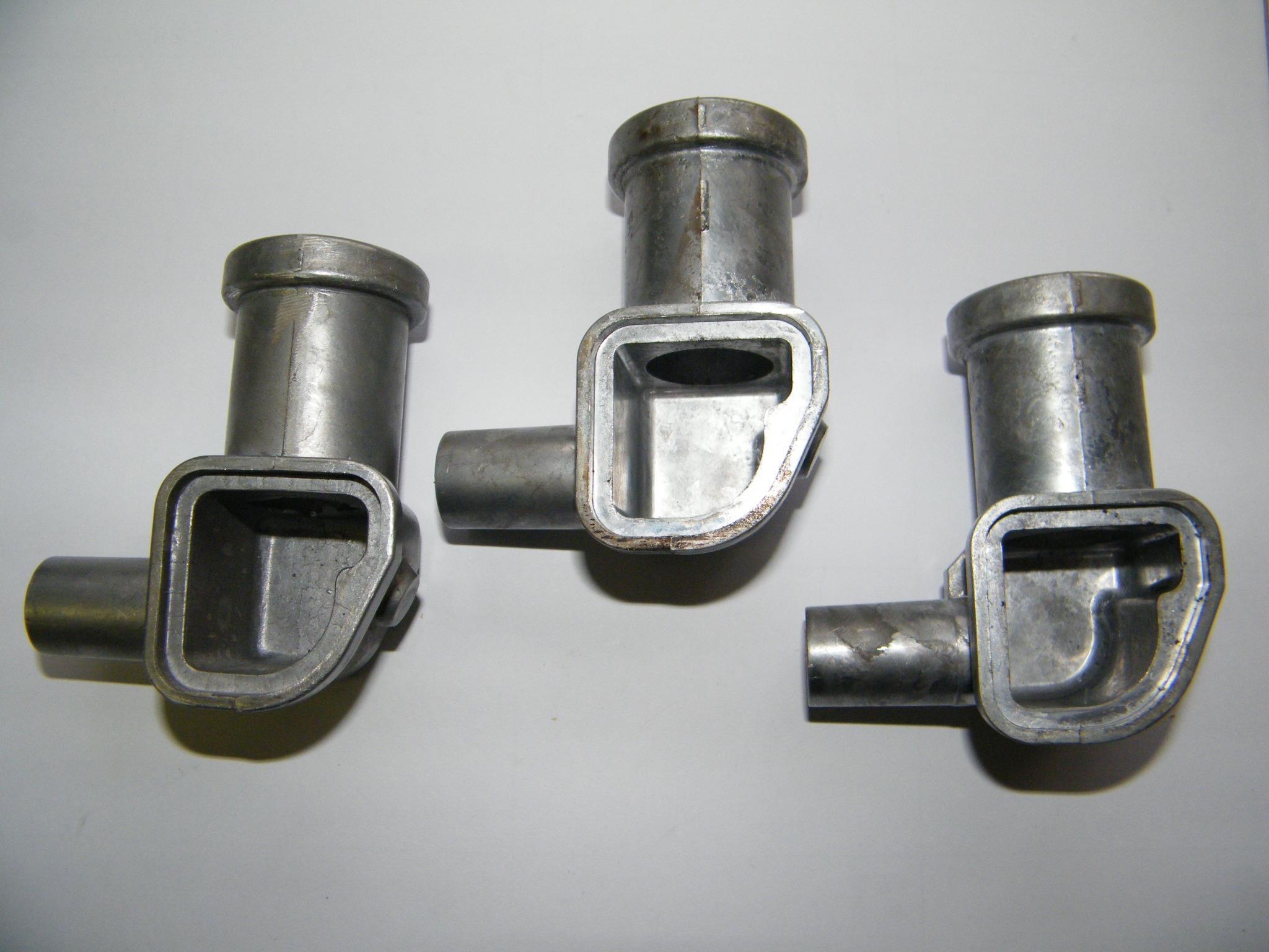 Carpenter Die Casting Three metal pipe fittings with rectangular and cylindrical openings are placed on a white surface.