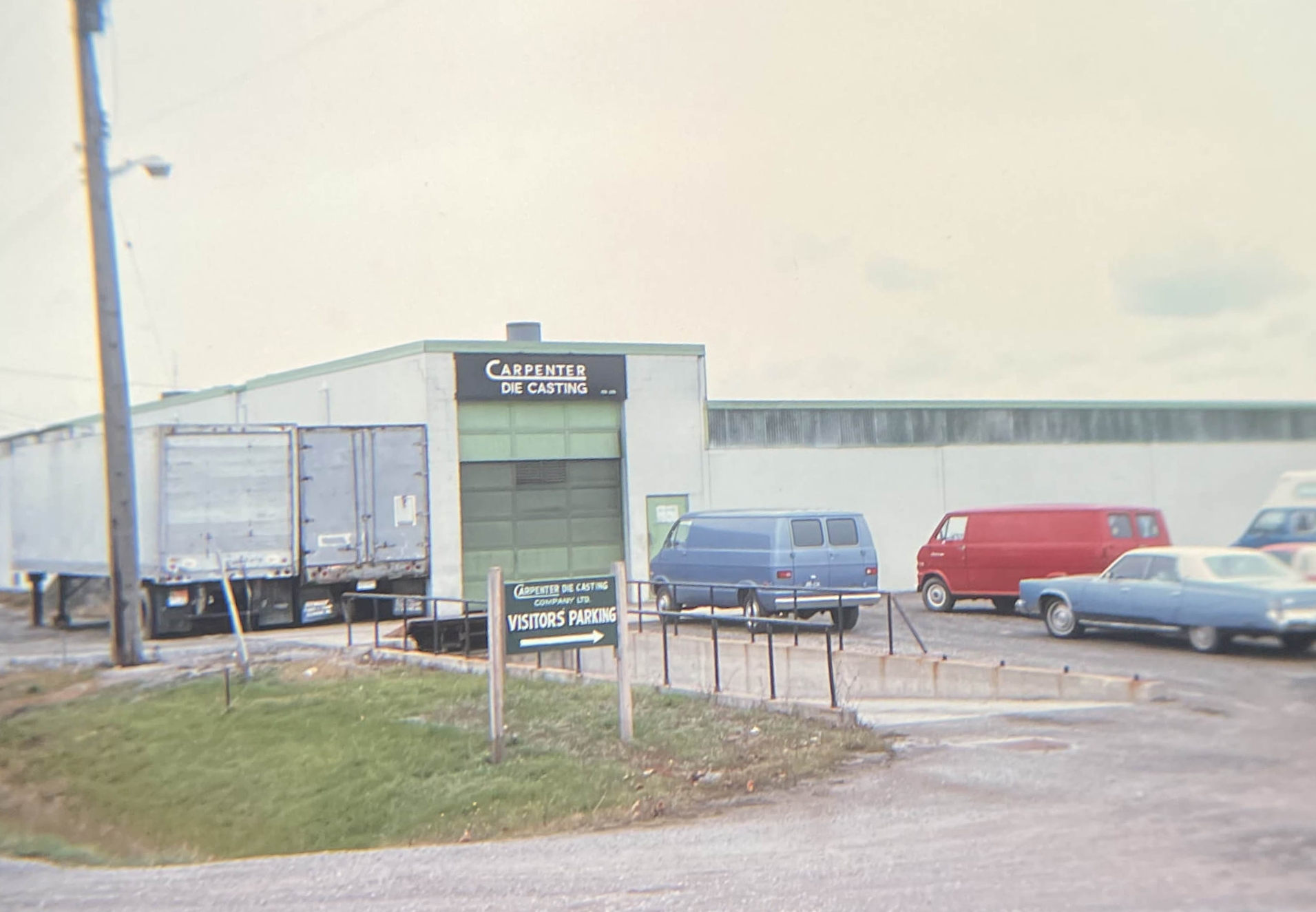 Carpenter Die Casting A parking lot with several vehicles in front of a building labeled "Carpenter Die Casting" and a sign that says "Visitors Parking.